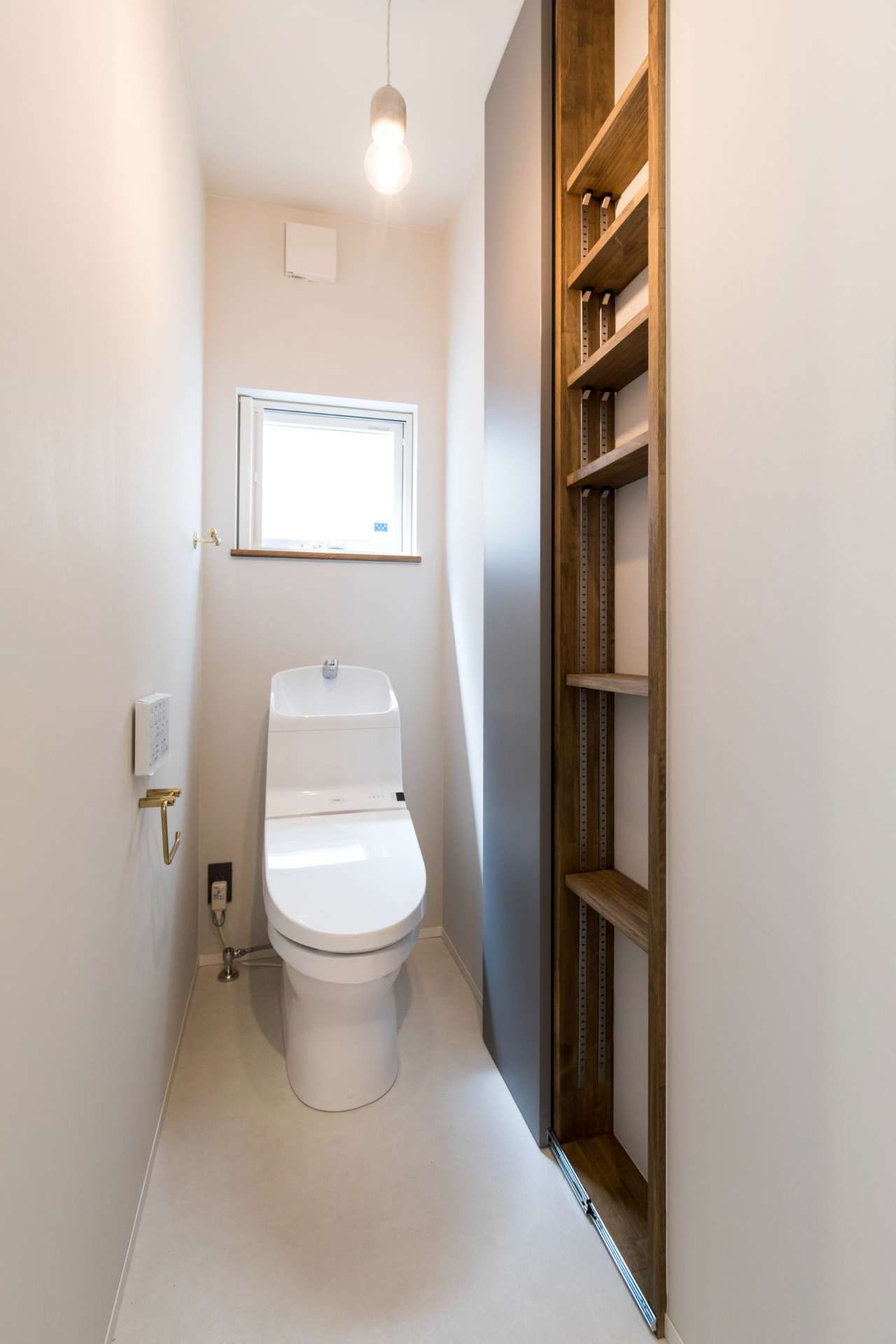 【1F　トイレ】<br>シンプルにまとまったトイレはこだわって選んだ真鍮のアクセサリーが良く映える空間に。<br>スライド式のハイドアを使用し、床から天井までの大容量のニッチ収納を造作。